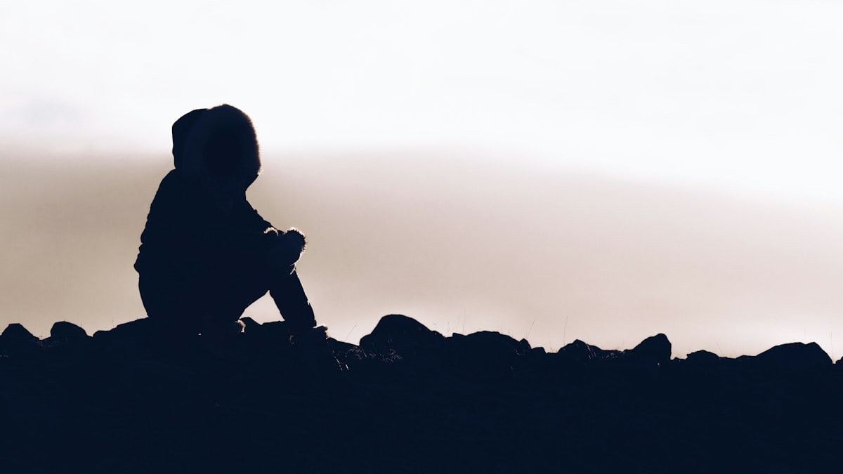 silhouette of man sitting on rock during sunset